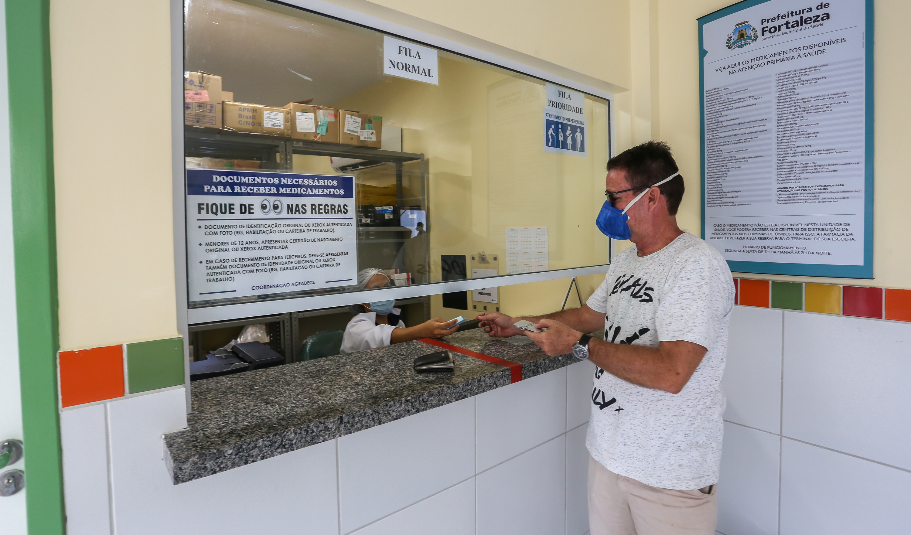 homem usando máscara em pé sendo atendido em recepção de posto de saúde